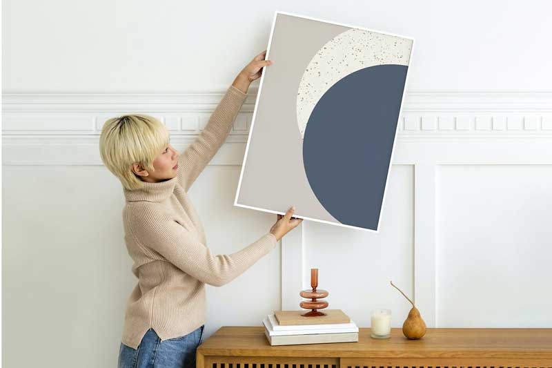 Woman hanging a photo frame on a white wall mockup
